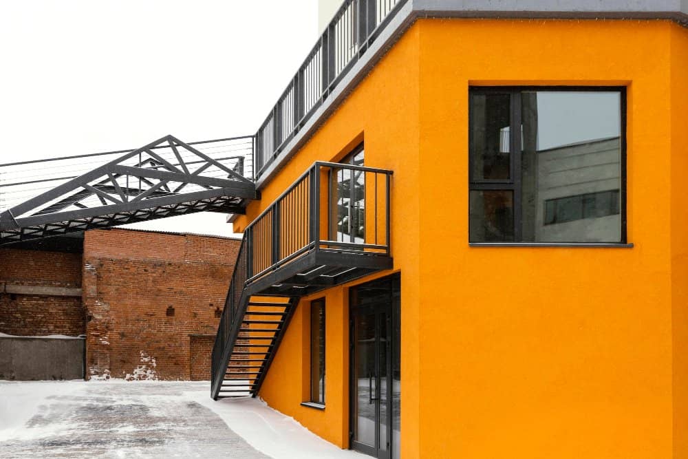 Modern orange exterior of a building with black metal balcony and staircase, showcasing innovative design and construction for home renovations.