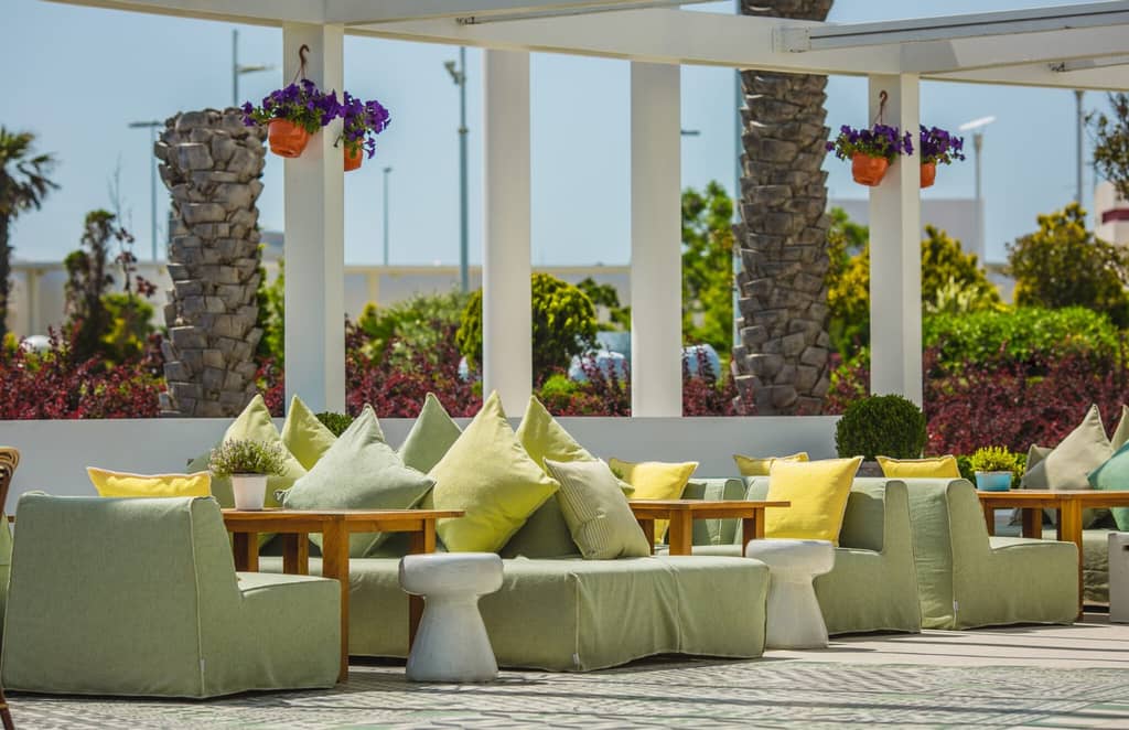 Modern outdoor seating area with green and yellow cushions, wooden tables, and decorative potted plants, ideal for enhancing outdoor living spaces in residential designs by Tekton Exteriors Mississippi.