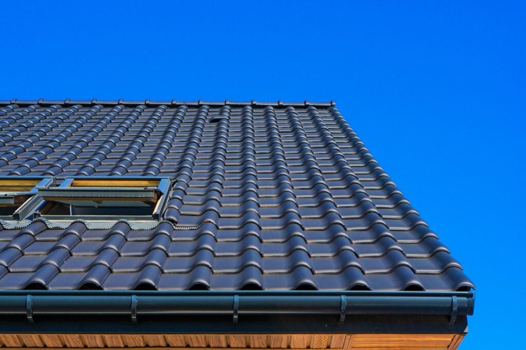 Roofing installation featuring durable black tiles and skylights against a clear blue sky, showcasing quality craftsmanship by Tekton Exteriors Mississippi.