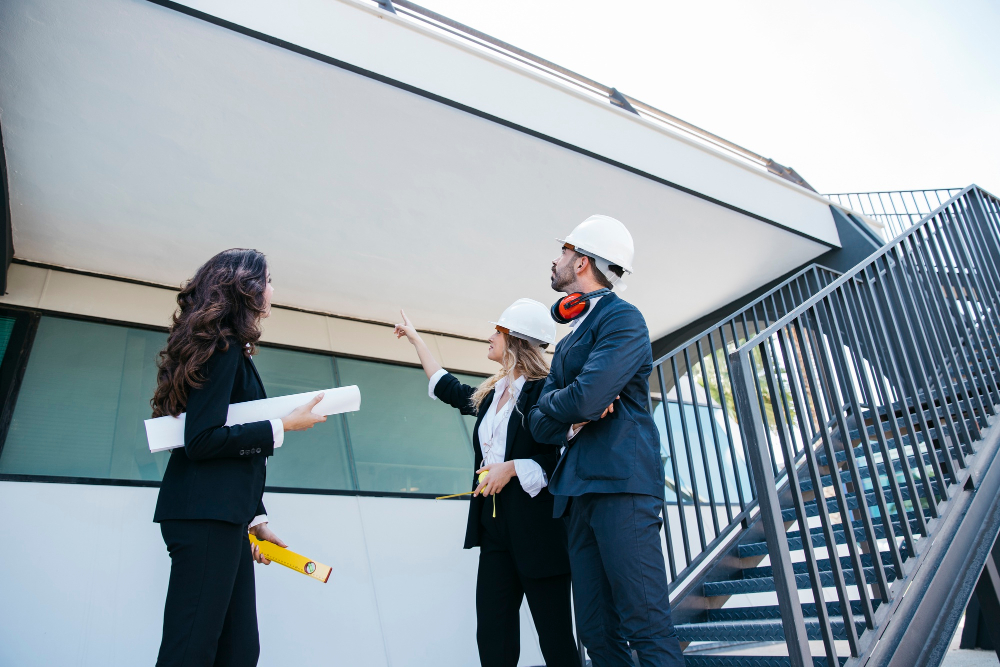 Professionals discussing construction plans at a building site, wearing hard hats and holding blueprints, emphasizing teamwork and architectural design.