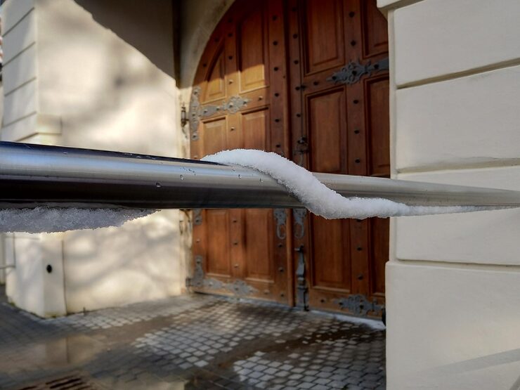 Close-up of snow accumulation on a metal railing in front of a wooden door, emphasizing winter conditions relevant to seamless gutters and water damage prevention.