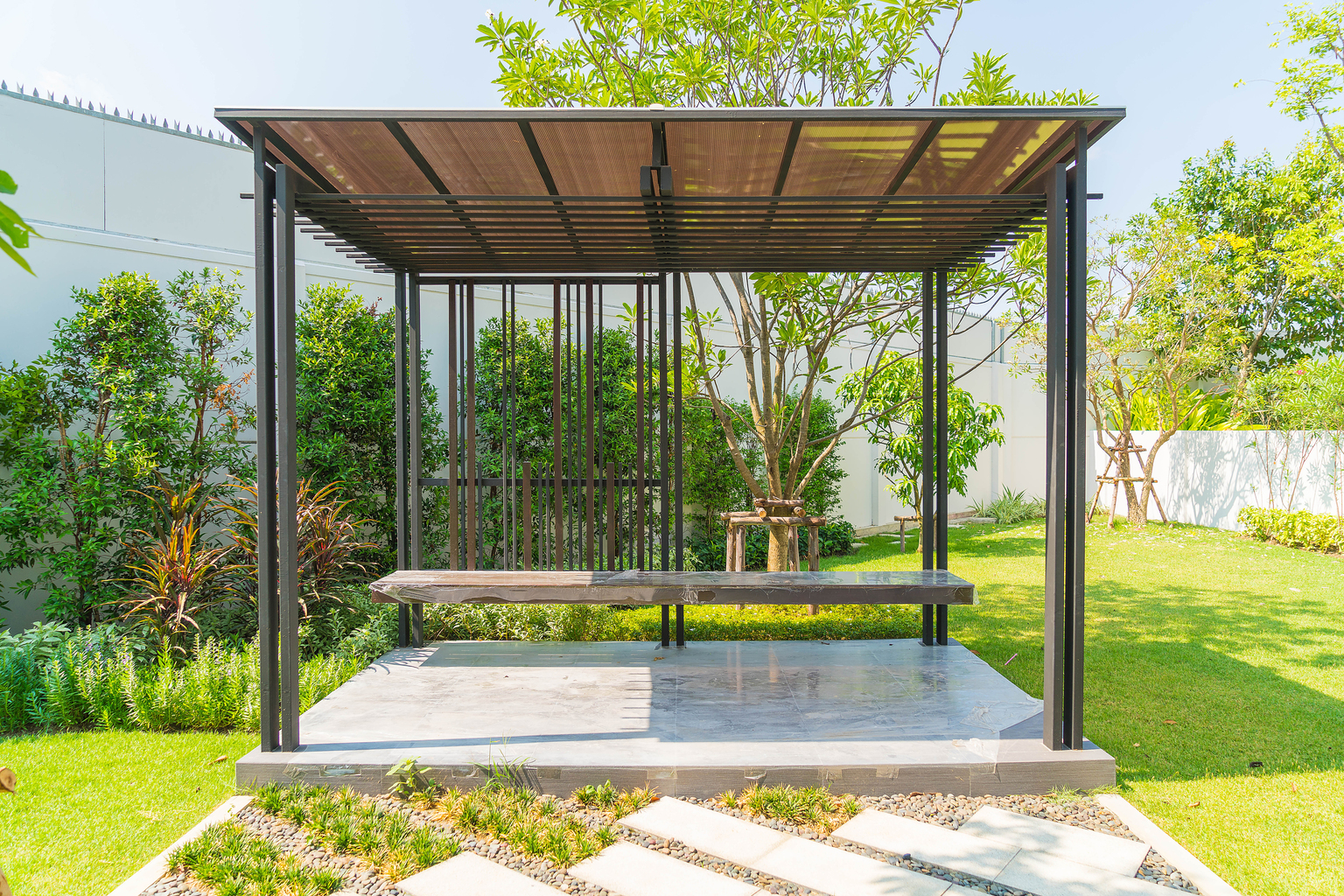 Aluminum pergola with modern design, featuring a sleek roof and a stone patio, surrounded by lush greenery, ideal for outdoor relaxation and shade in Mississippi's climate.