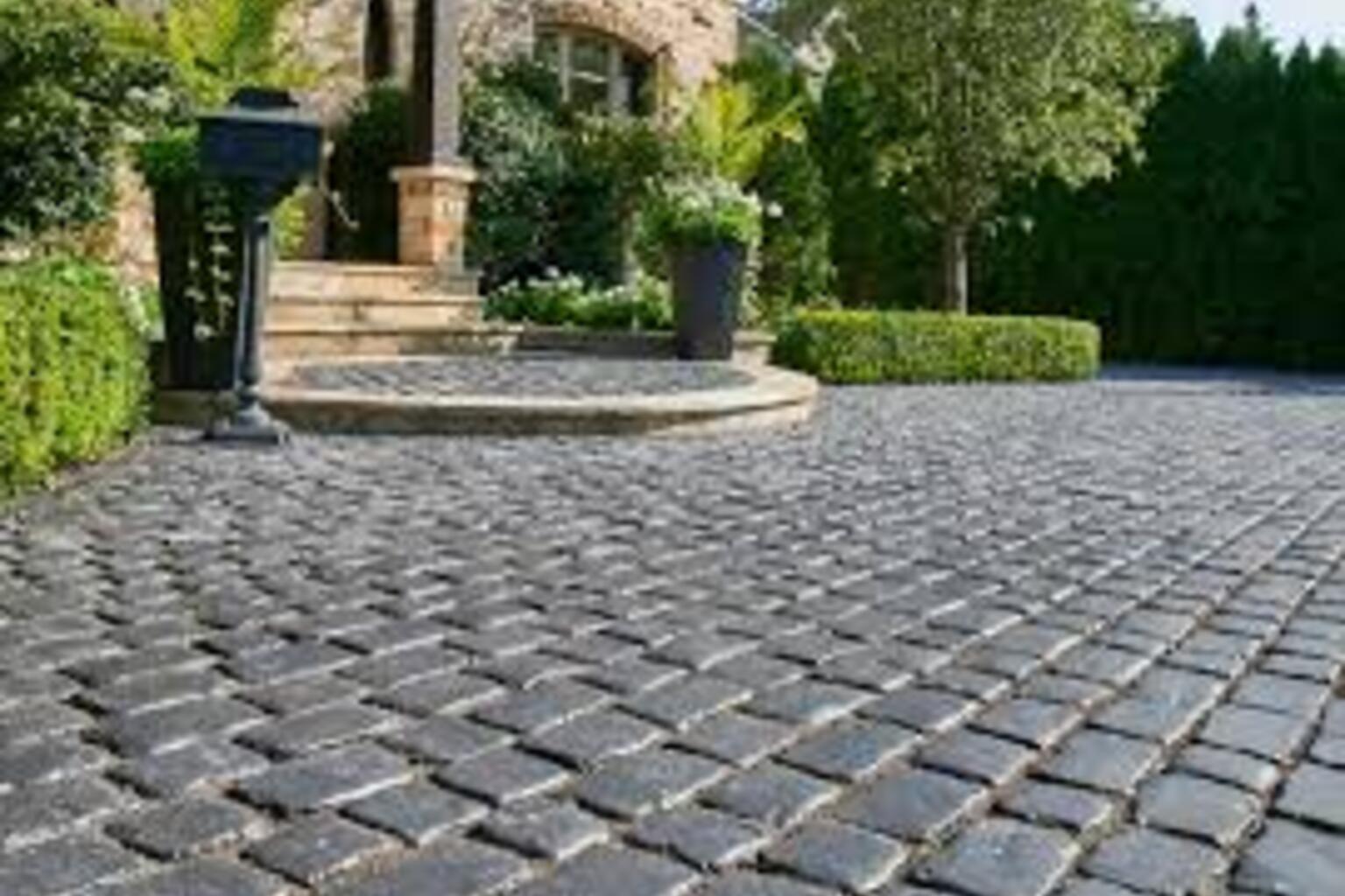 Cobblestone driveway with interlocking pavers, showcasing a durable and textured surface, surrounded by greenery and steps leading to a home entrance.