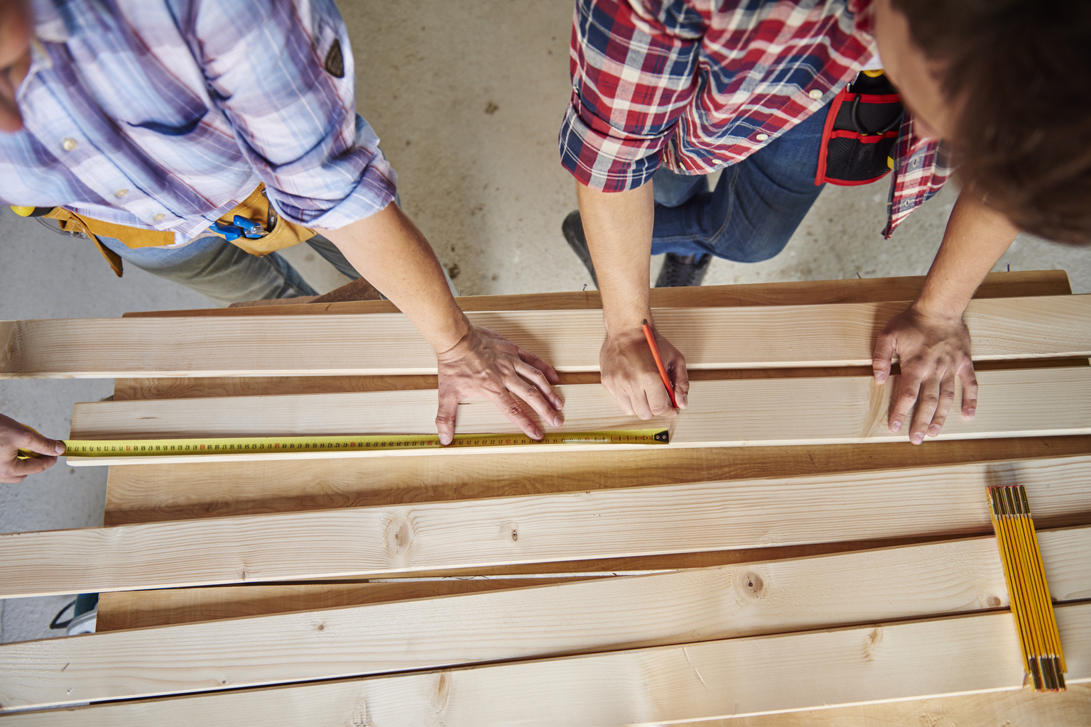 Two carpenters measuring and marking cedar and pressure-treated pine boards for deck construction, showcasing craftsmanship and precision in outdoor project preparation.