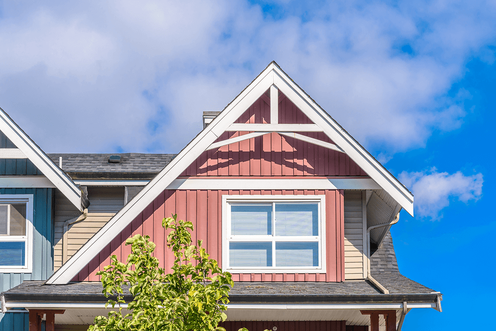 Colorful residential rooftop with gable architecture, showcasing a mix of blue and red siding under a bright blue sky, symbolizing quality craftsmanship in outdoor home design.