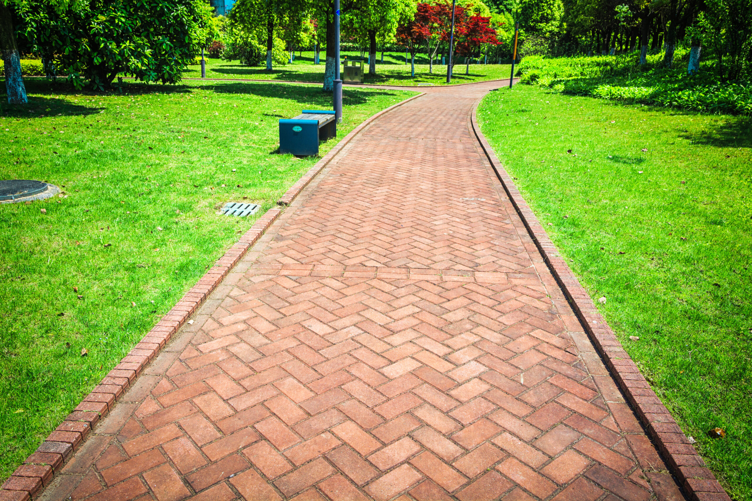 Permeable paver pathway in a city park, surrounded by lush green grass and trees, showcasing eco-friendly design and sustainable landscaping.