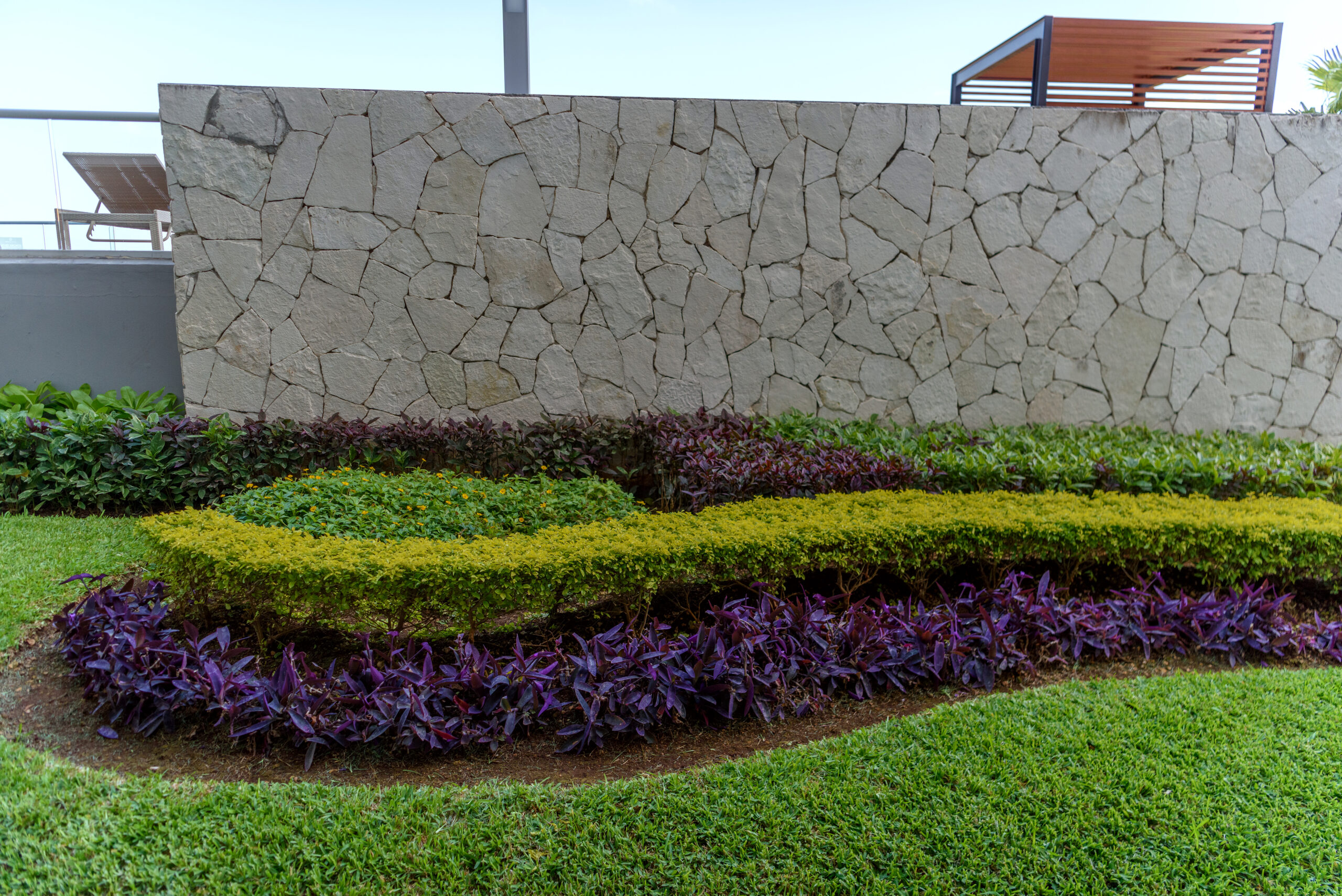 Decorative retaining wall made of natural stone with colorful garden beds featuring green and purple foliage, enhancing outdoor space aesthetics.
