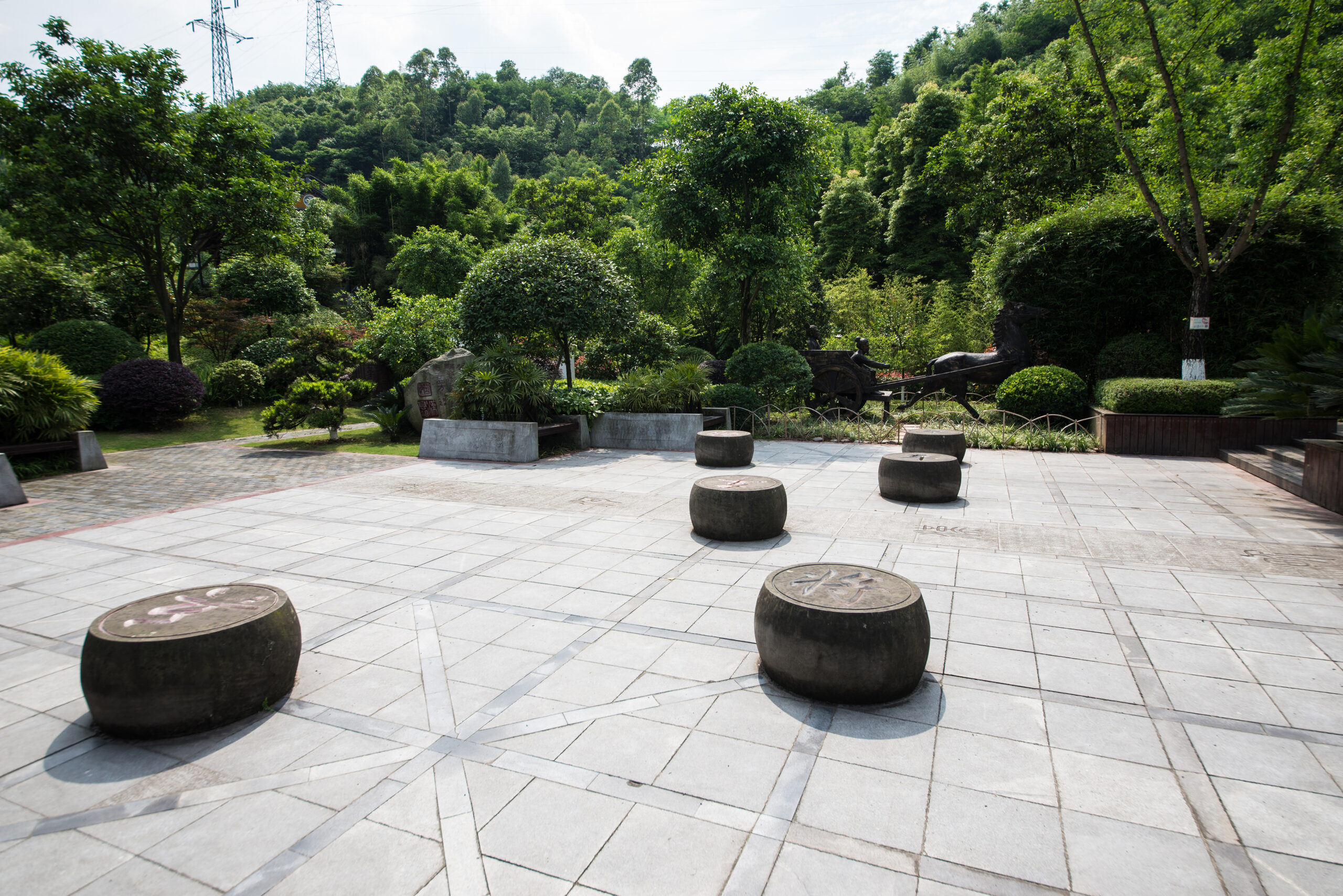 Stone seating elements arranged in a park setting, surrounded by lush greenery and designed for outdoor relaxation and entertainment, reflecting the craftsmanship and aesthetic appeal of Tekton Exteriors' custom stone bench installations.