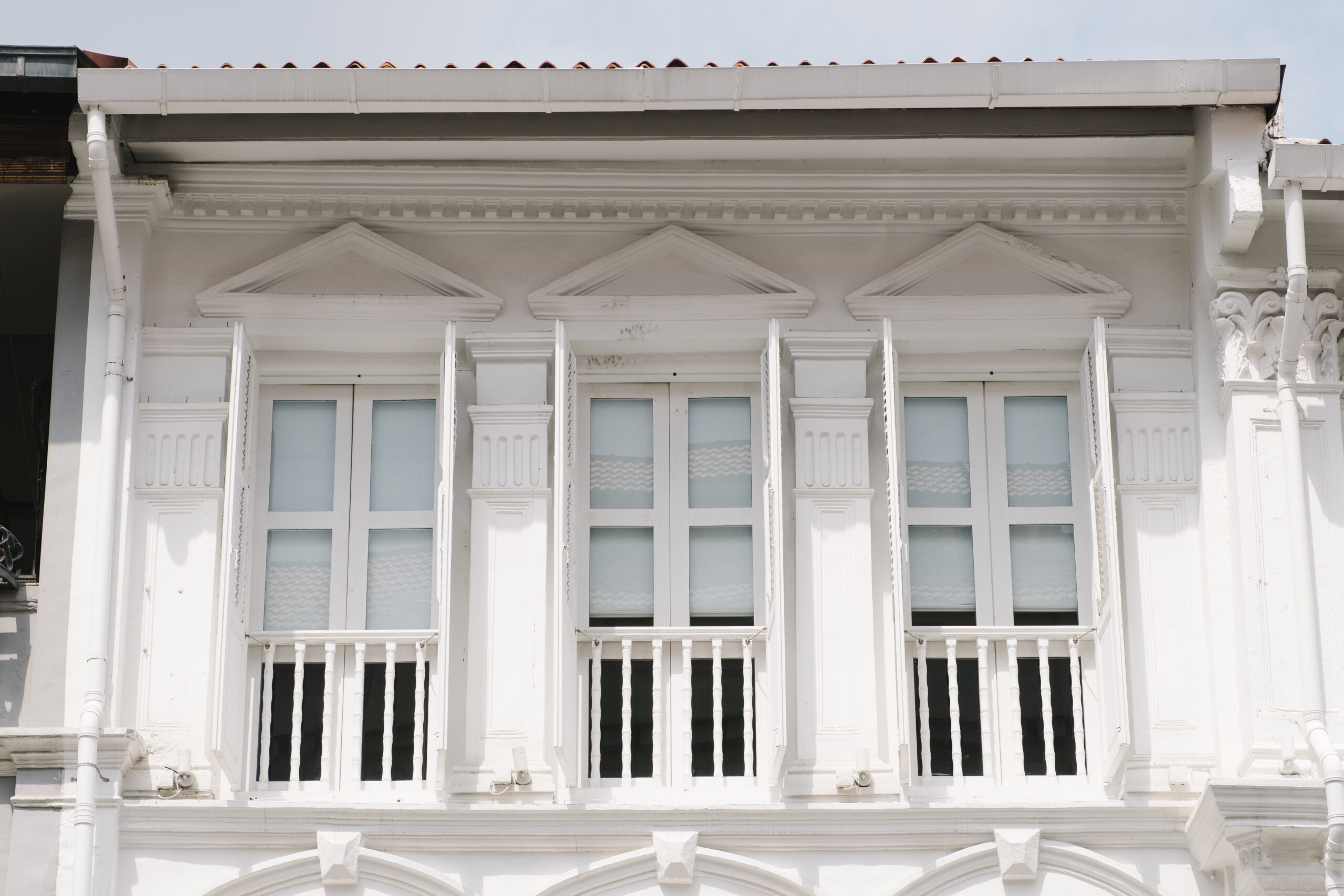 Colonial-style building featuring elegant white Pella casement windows with decorative shutters and intricate architectural details, emphasizing energy efficiency and aesthetic appeal.