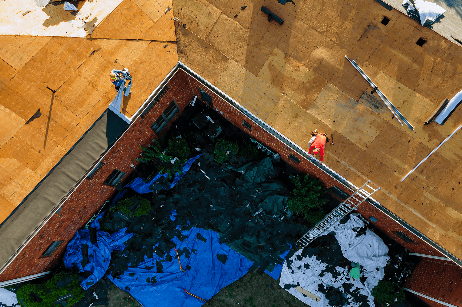 Roofing crew working on a house, with new wooden shingles installed and debris in the yard, illustrating roof replacement services.