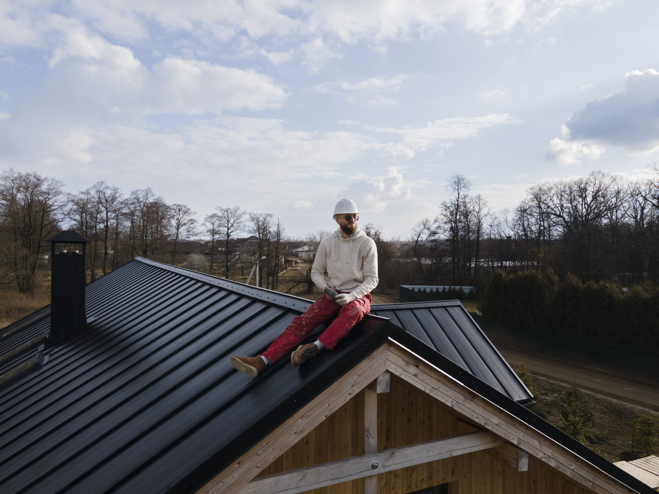 Man wearing a safety helmet sitting on a black metal roof, showcasing roofing expertise and safety in construction.