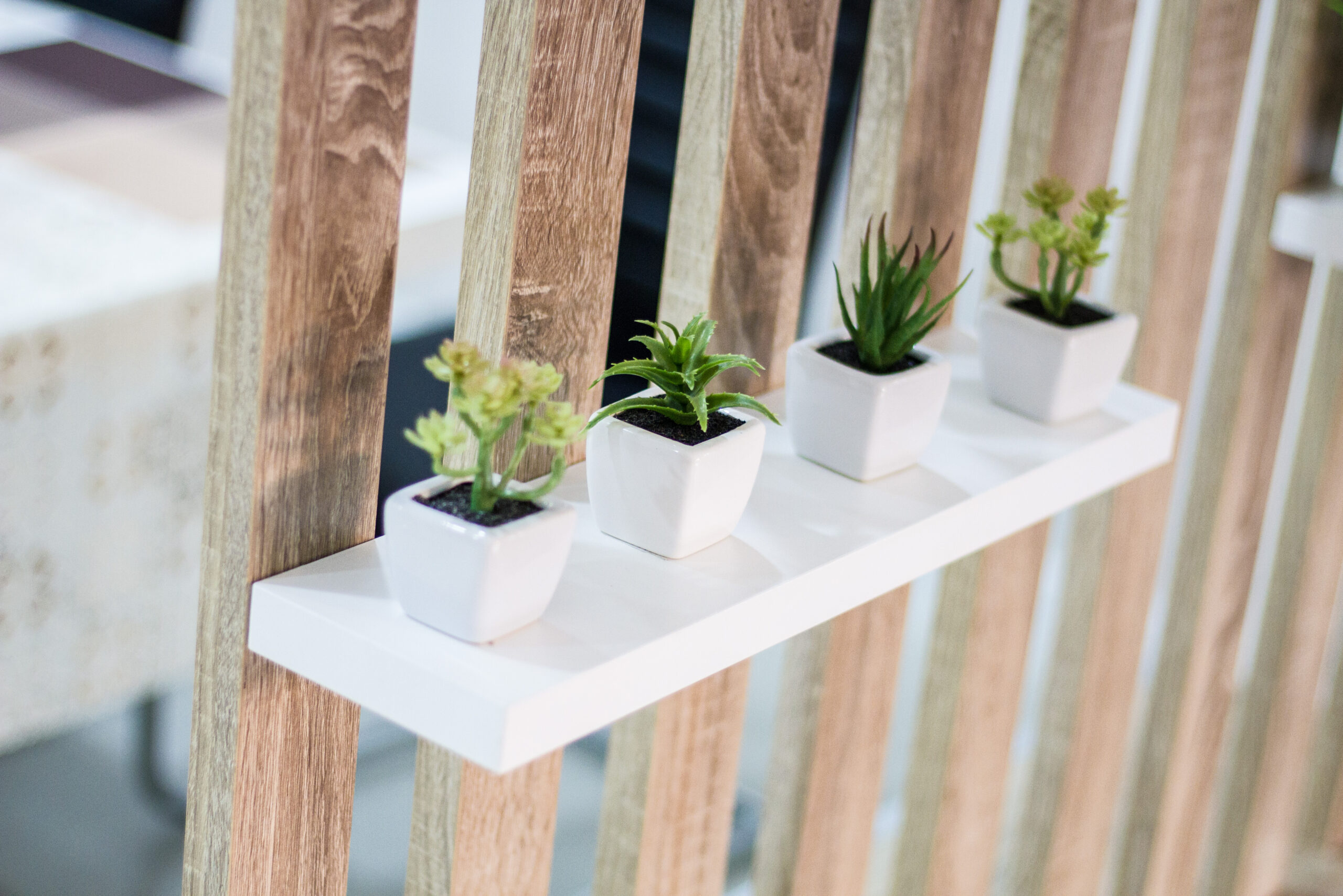 Potted plants in white containers on a modern shelf against a wooden railing, illustrating decorative gardening solutions for outdoor spaces by Tekton Exteriors Mississippi.