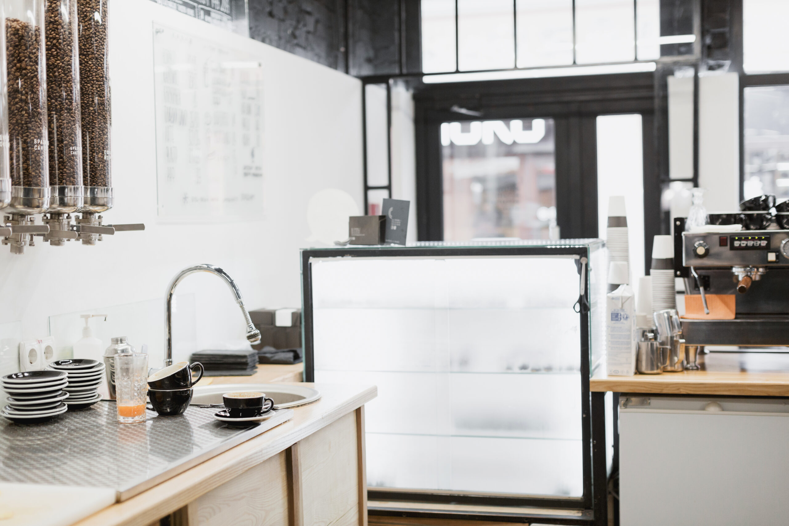 Coffee shop interior featuring a sleek counter with coffee beans in glass containers, stacked plates, and cups, highlighting a modern aesthetic and inviting atmosphere.