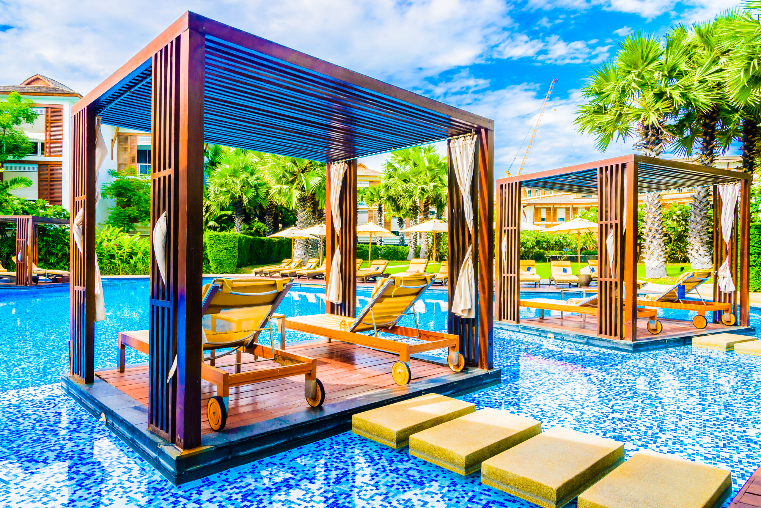 Luxury outdoor cabanas by a pool surrounded by tropical greenery, emphasizing relaxation and comfort in a stylish outdoor living space.