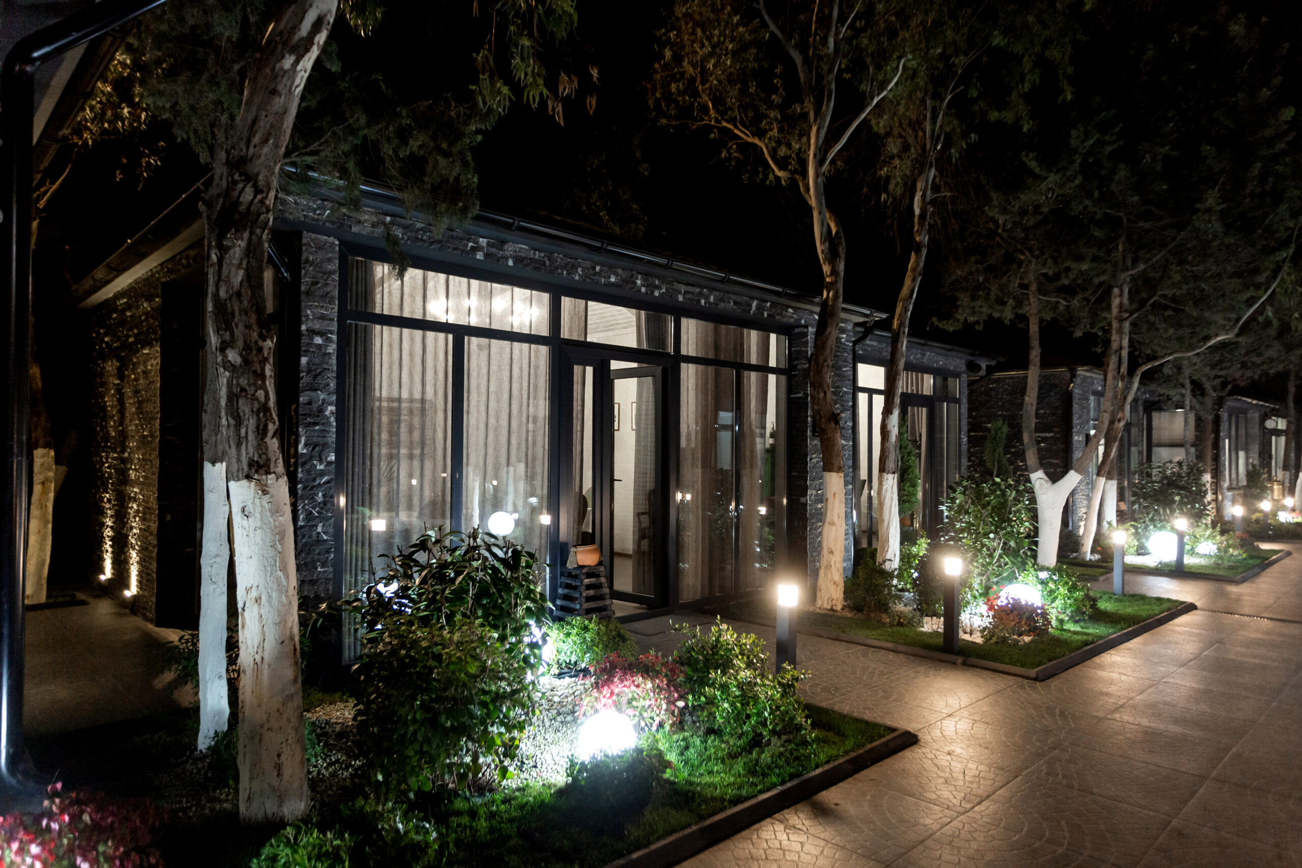 Outdoor restaurant cottage illuminated with professional uplighting, showcasing landscaped gardens and accentuating architectural features at night.
