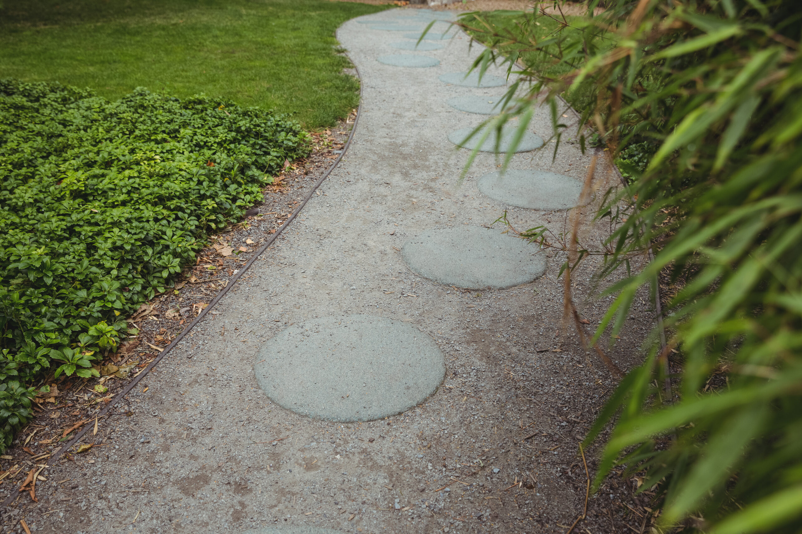 Curved garden pathway featuring circular stepping stones surrounded by lush greenery, illustrating custom walkway design by Tekton Exteriors Mississippi.